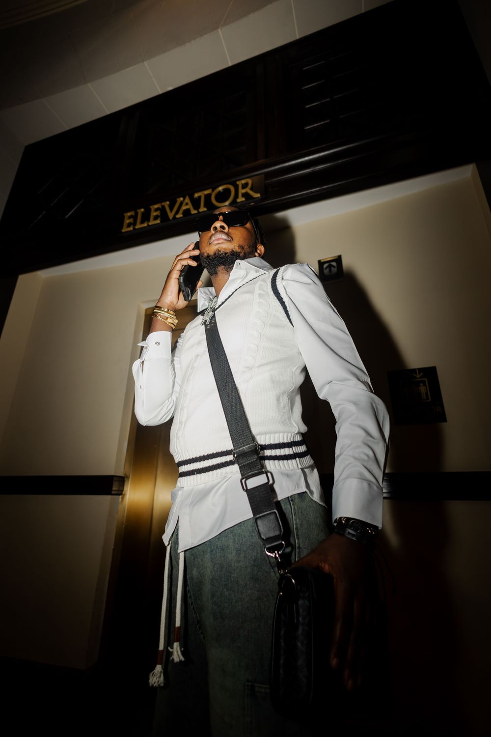 Person in white clothing photographed from dramatic angles near an elevator sign.