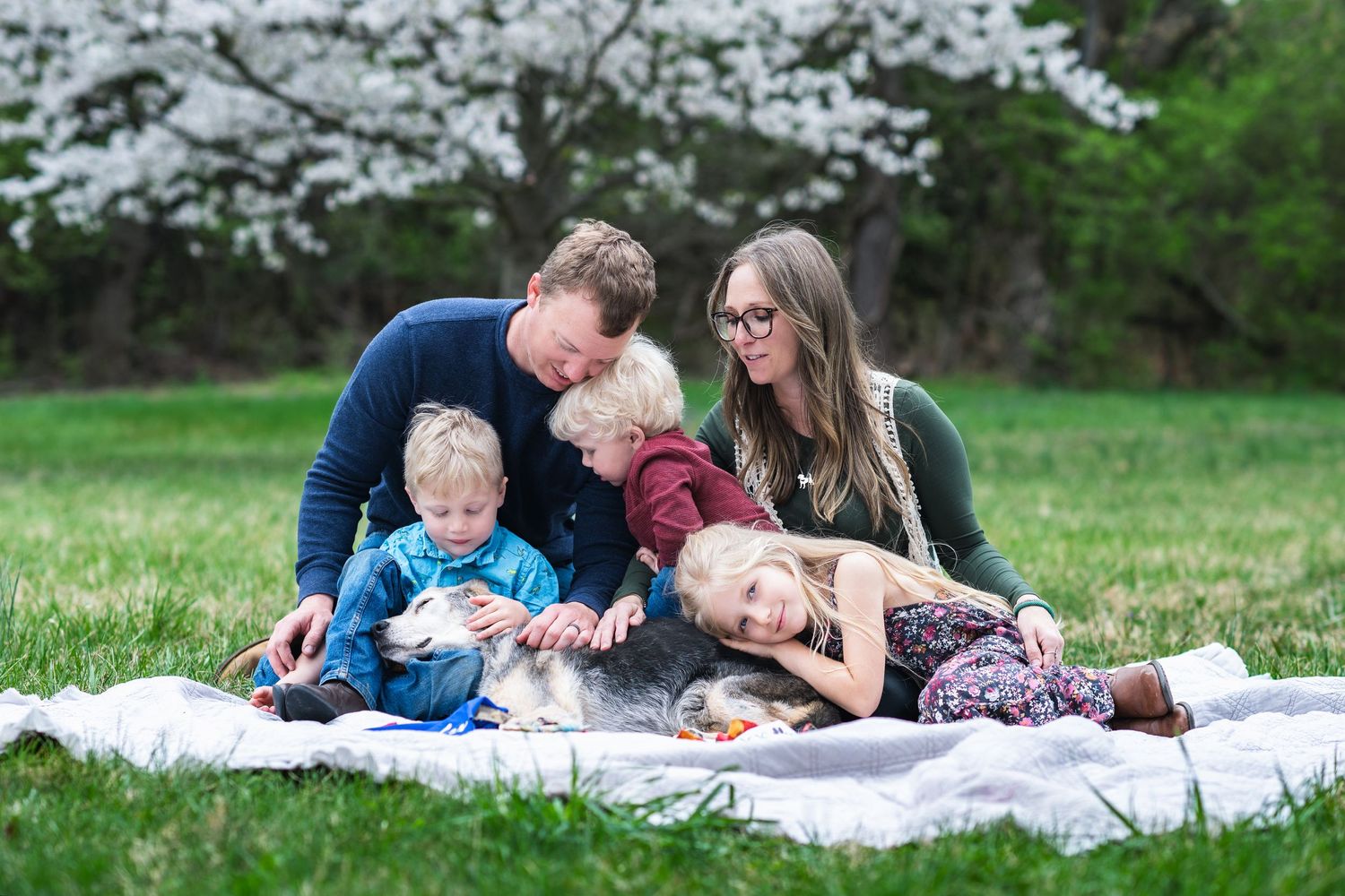 A family enjoys quality time together while relaxing on a blanket in a spring garden with blooming trees.