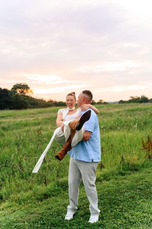 A couple shares an intimate dance together in a lush green meadow at sunset.