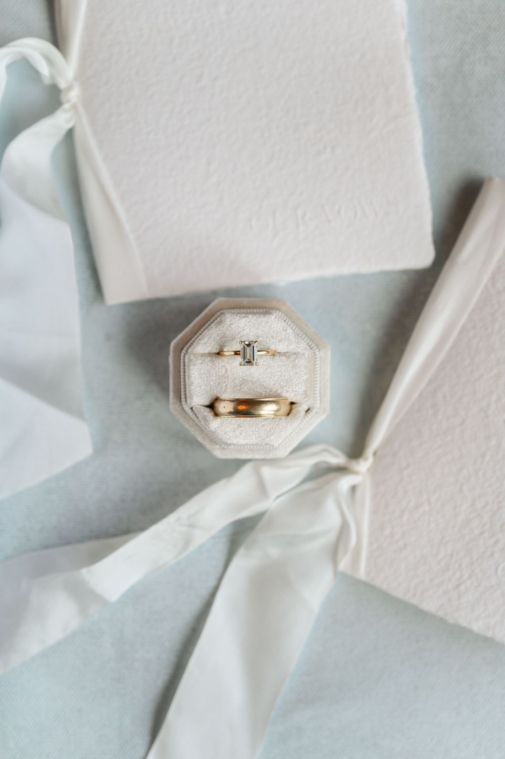 Wedding rings displayed in an octagonal velvet ring box against white fabric and ribbon.