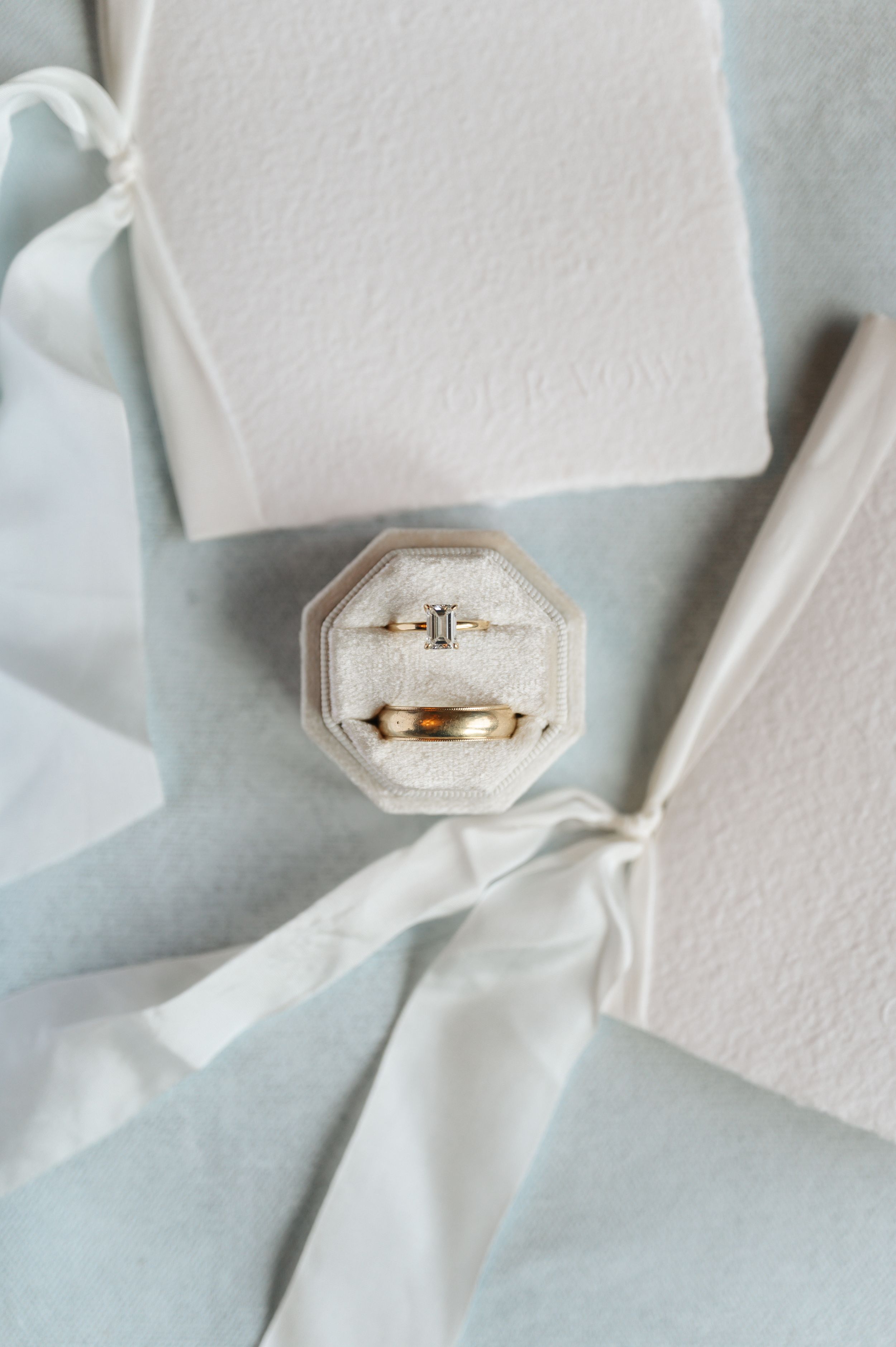 Wedding rings displayed in an octagonal velvet ring box against white fabric and ribbon.
