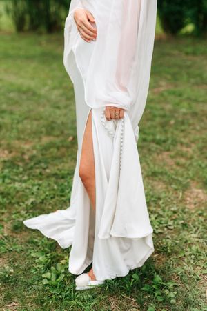 Close-up details of a flowing white wedding dress and bare feet on grass create an artistic bridal portrait series.