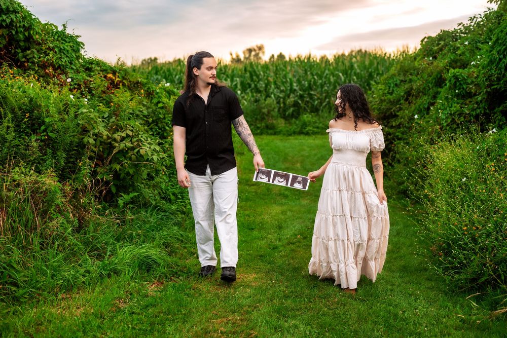 Couple walking hand in hand through a lush garden path at sunset holding baby shoes.