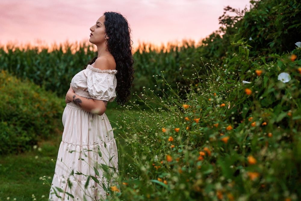 Woman in white dress standing in garden at sunset with orange wildflowers.