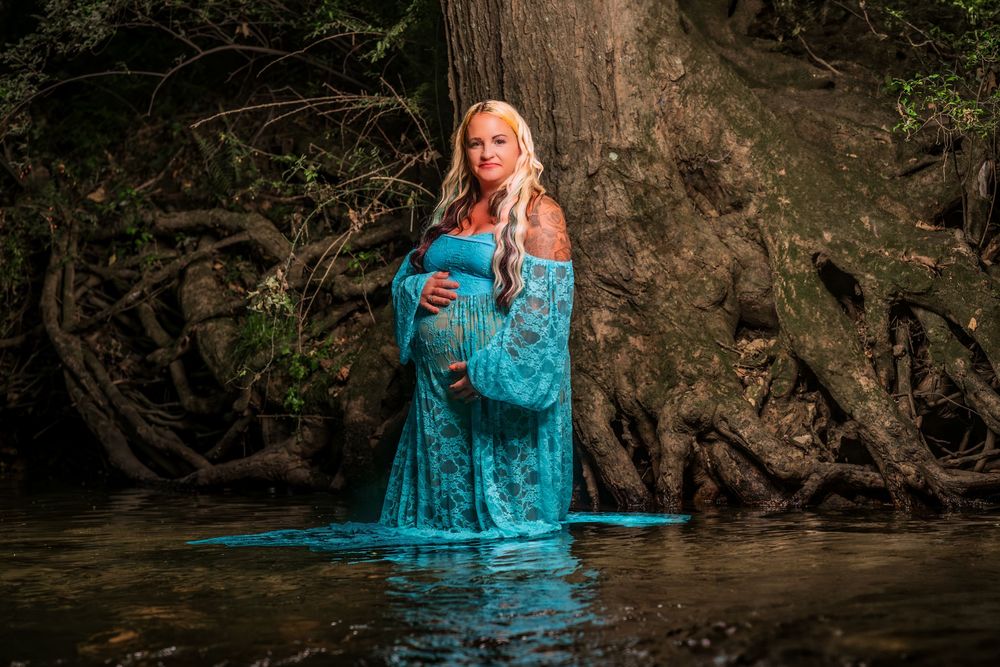 Maternity portrait in turquoise dress standing in forest stream with exposed tree roots.