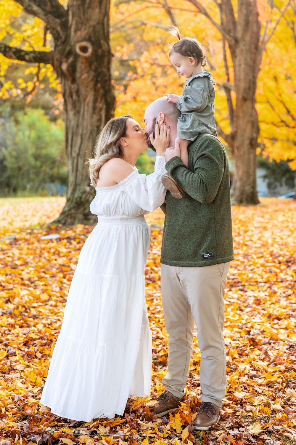 A couple dances together in a park filled with vibrant yellow autumn leaves and trees.
