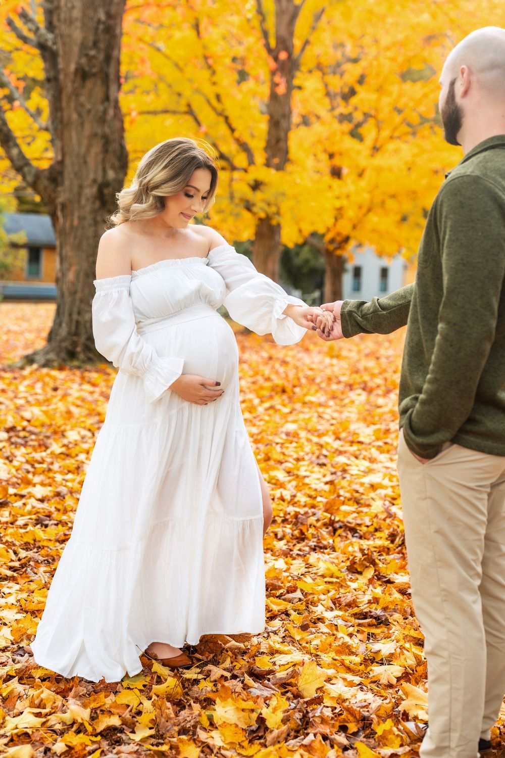 Couple in white dress and casual wear pose among fallen autumn leaves.