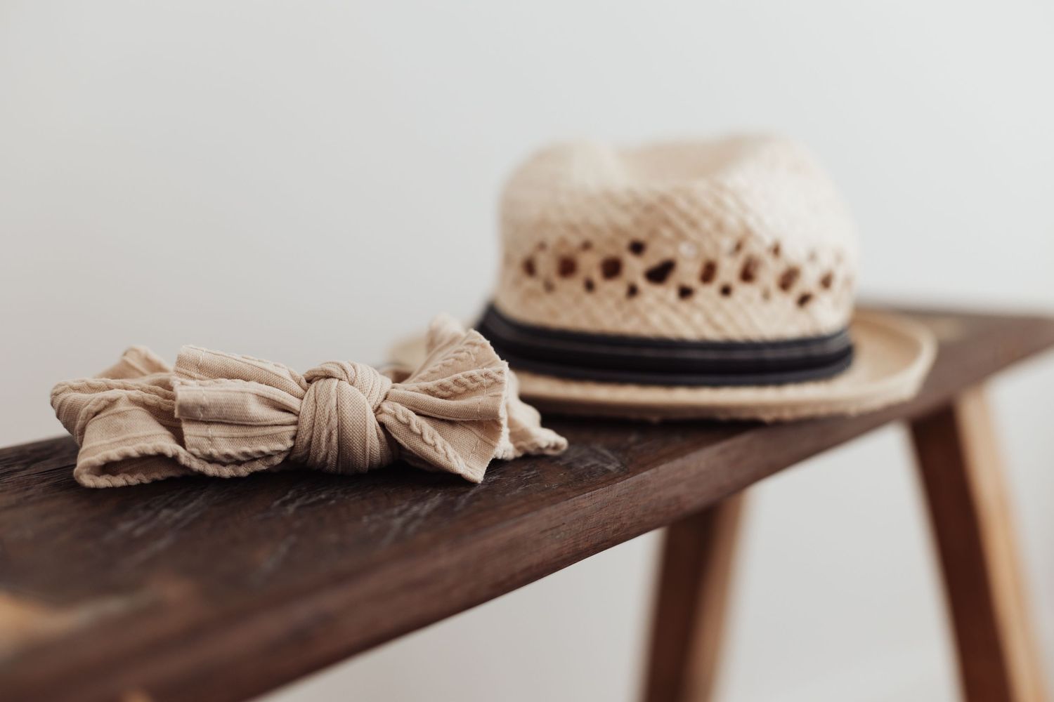 A straw sunhat with black band and beige bow accessories rest on a wooden surface in soft natural light.