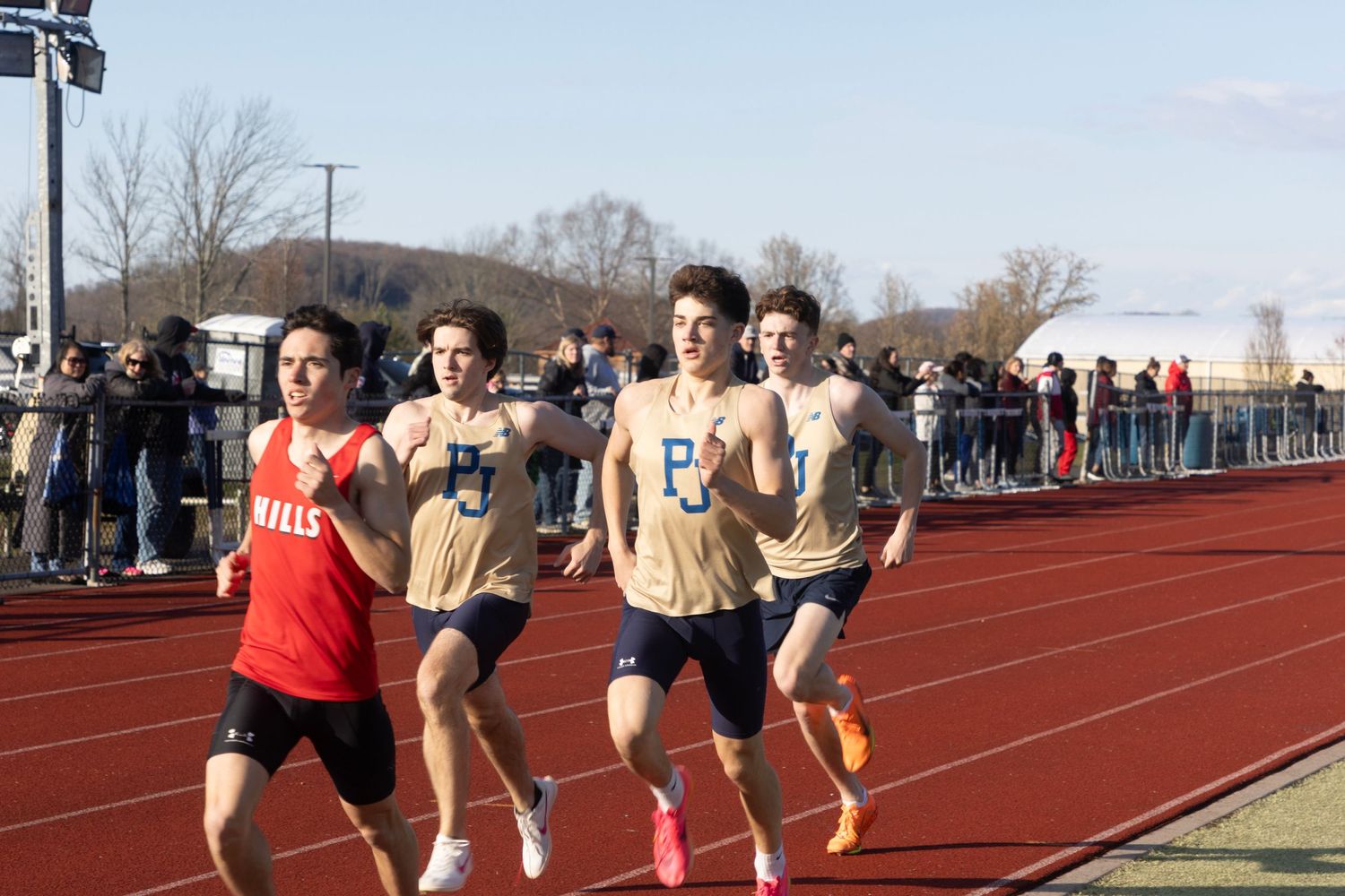 Male track athletes compete in a distance running race on an outdoor track.