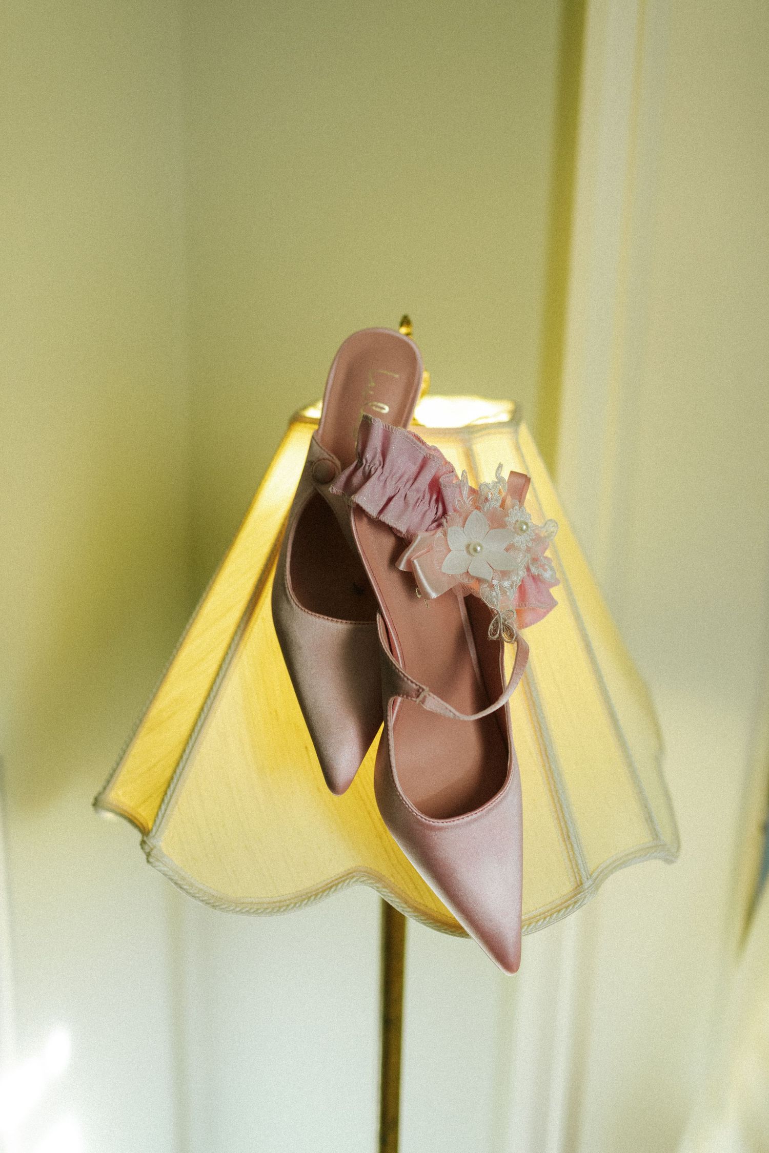 Two pink shoes and a pink garter hang on the shade of a vintage lamp