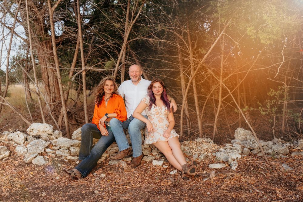 A group pose on rocks at sunset in a wooded area with golden light filtering through bare branches.