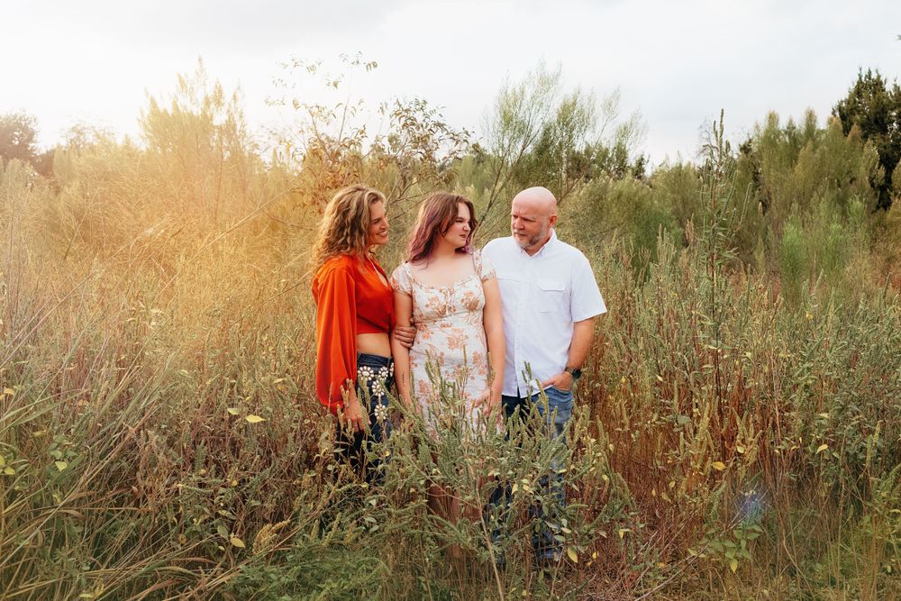 Three people stand together in a sunlit field of tall grass during golden hour.