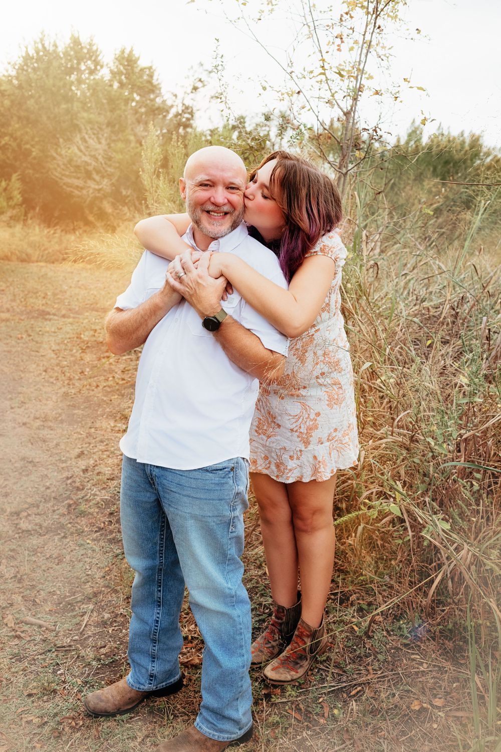 A loving embrace between two people on a nature path with warm sunset lighting in the background.
