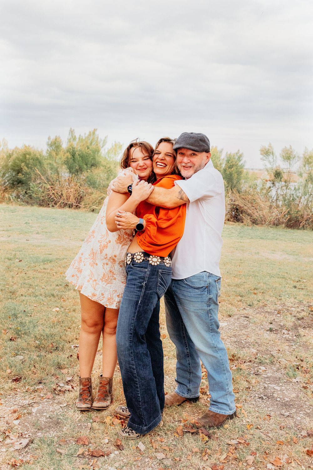 A group of three people sharing a joyful hug outdoors on a cloudy day.