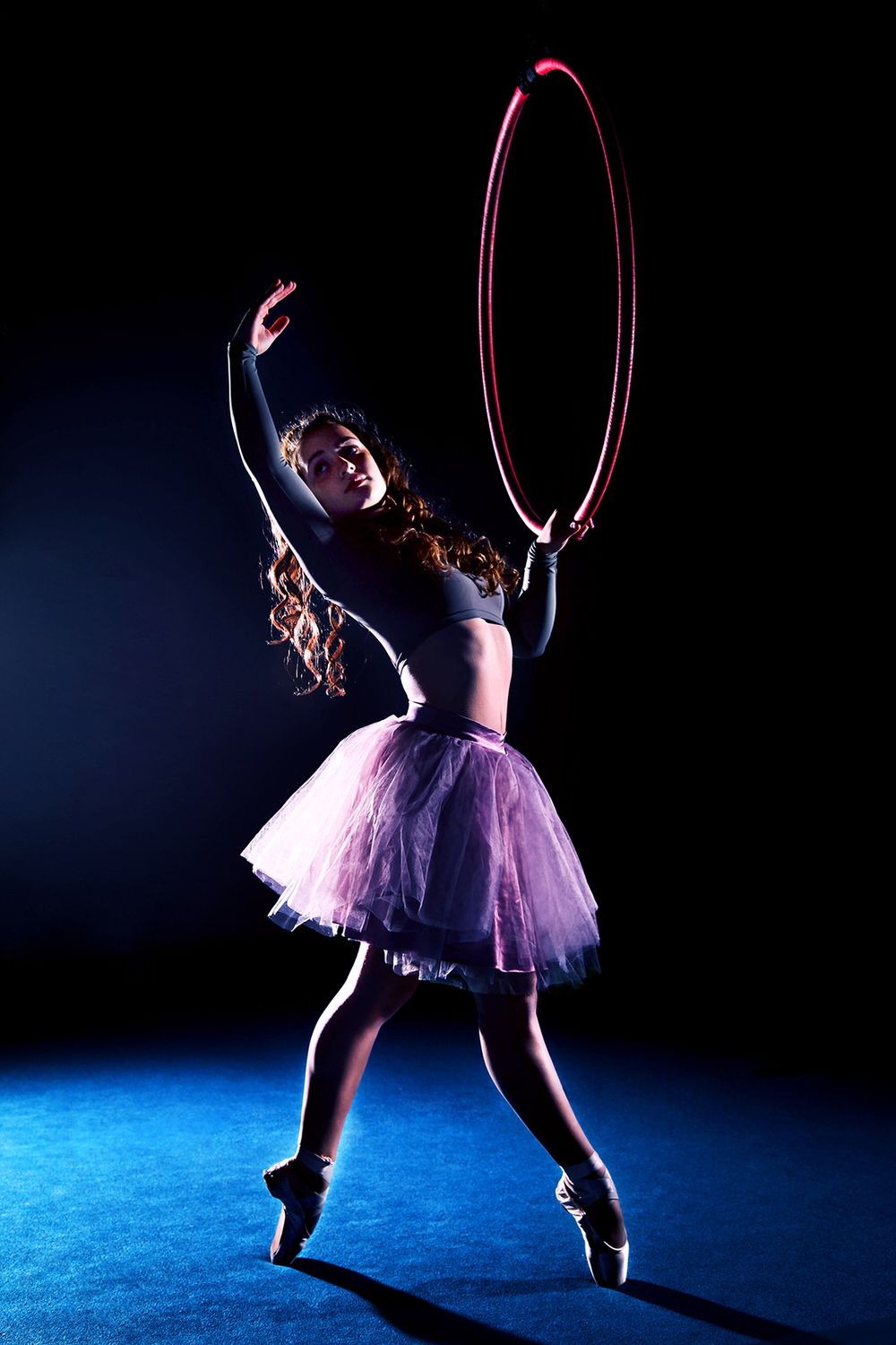 A dancer performs an elegant pose in a circus hoop against a dark background with dramatic lighting. (Chili, New York)