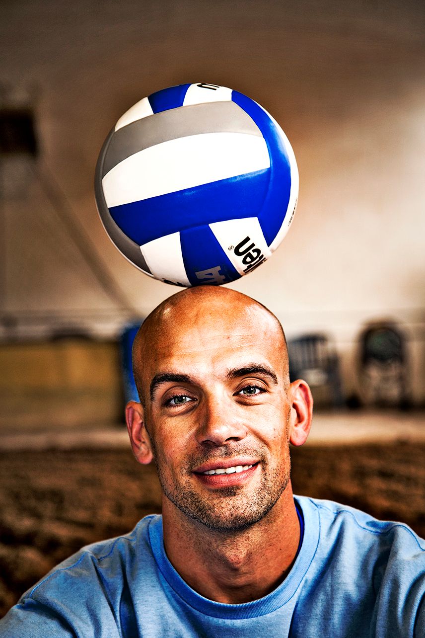 A blue and white volleyball balanced on top of a person wearing a light blue shirt against a blurry background. (Gates New York)