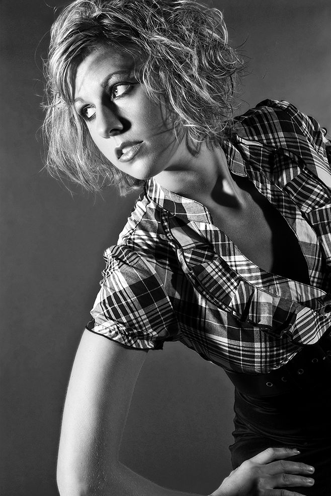 Black and white fashion portrait of a model in plaid shirt posing dramatically with tousled hair against dark backdrop. (Perinton New York)