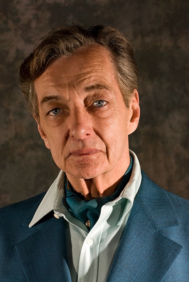 Portrait of a mature man wearing a blue suit jacket and white collared shirt against a dark textured background. (Clarkson NY)