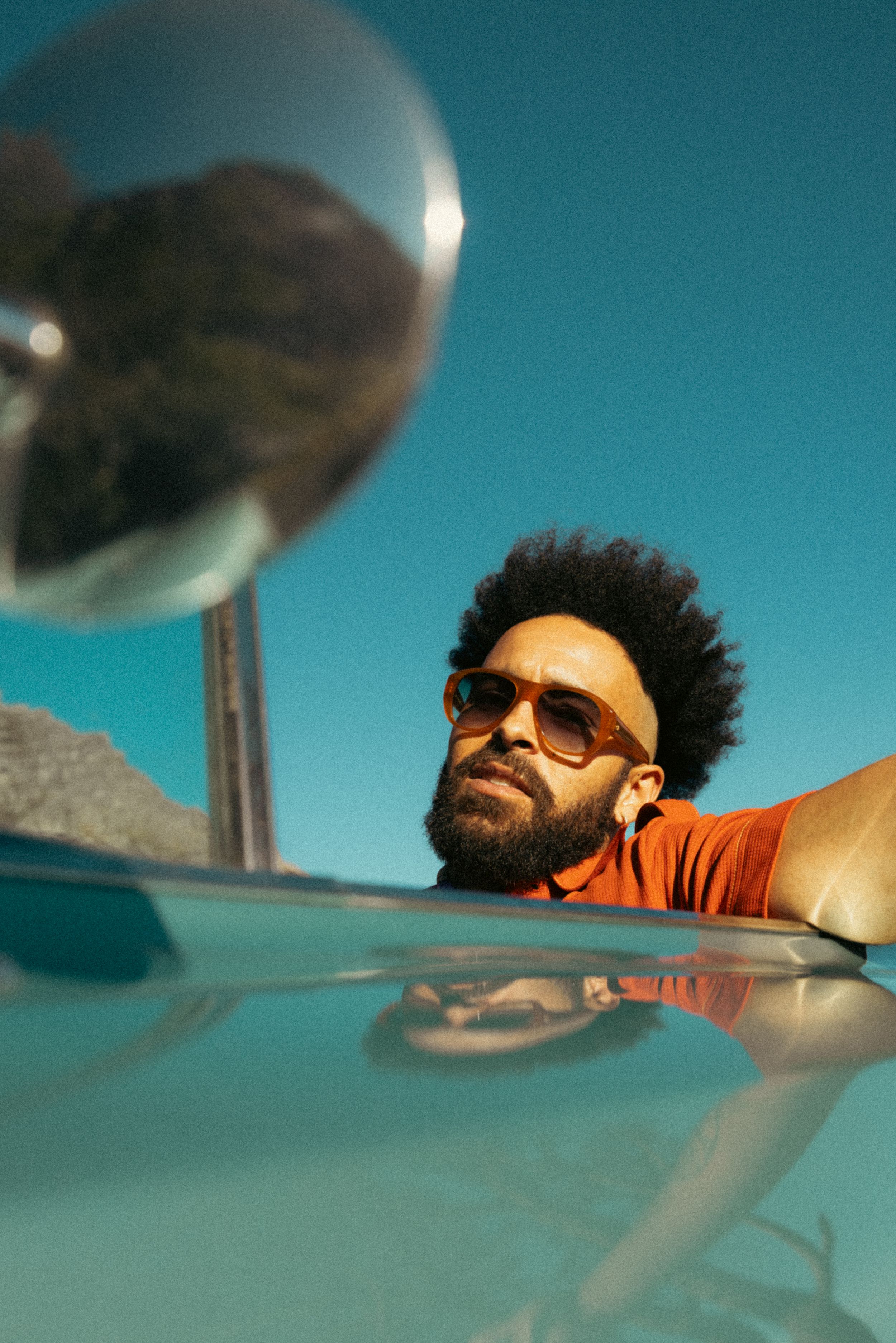 Stylish shot of person with sunglasses reflected in side mirror of car against vibrant blue sky.