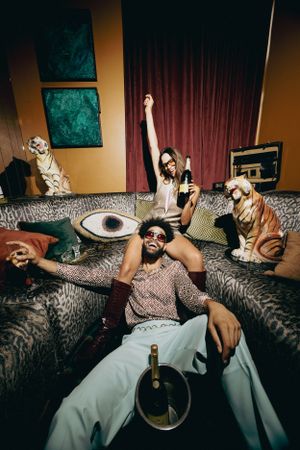 People relaxing on a couch with sunglasses and bottles of wine, surrounded by decorative tigers and artwork.