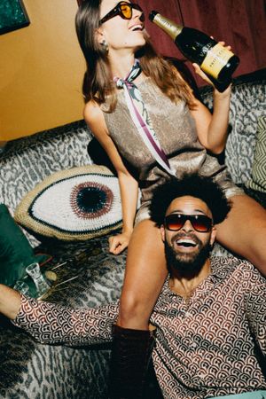 Friends lounging on a couch during a party with colorful sunglasses and decorative eye pillow.