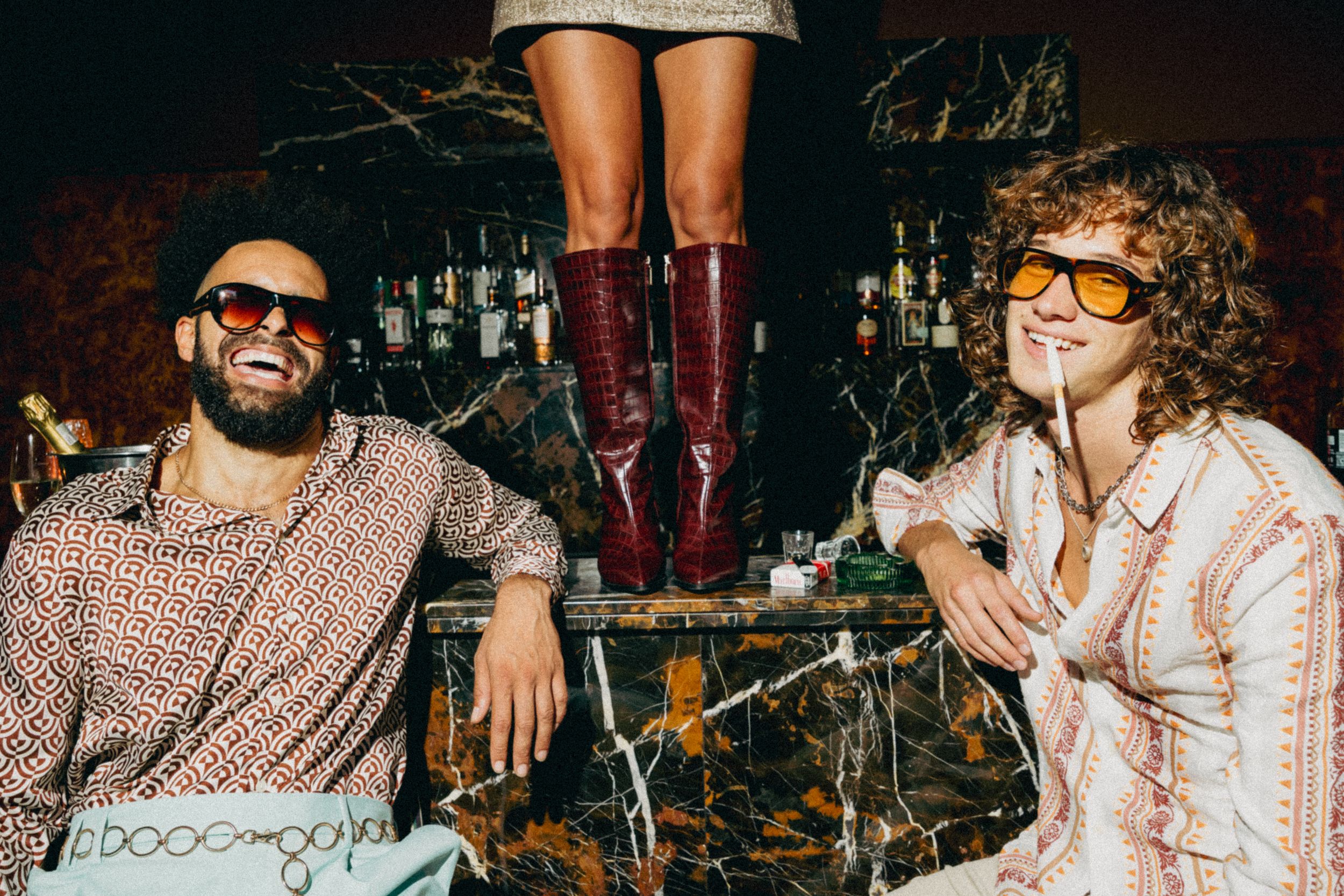 Two people smiling and relaxing in a casual setting with burgundy boots visible in the frame above them.