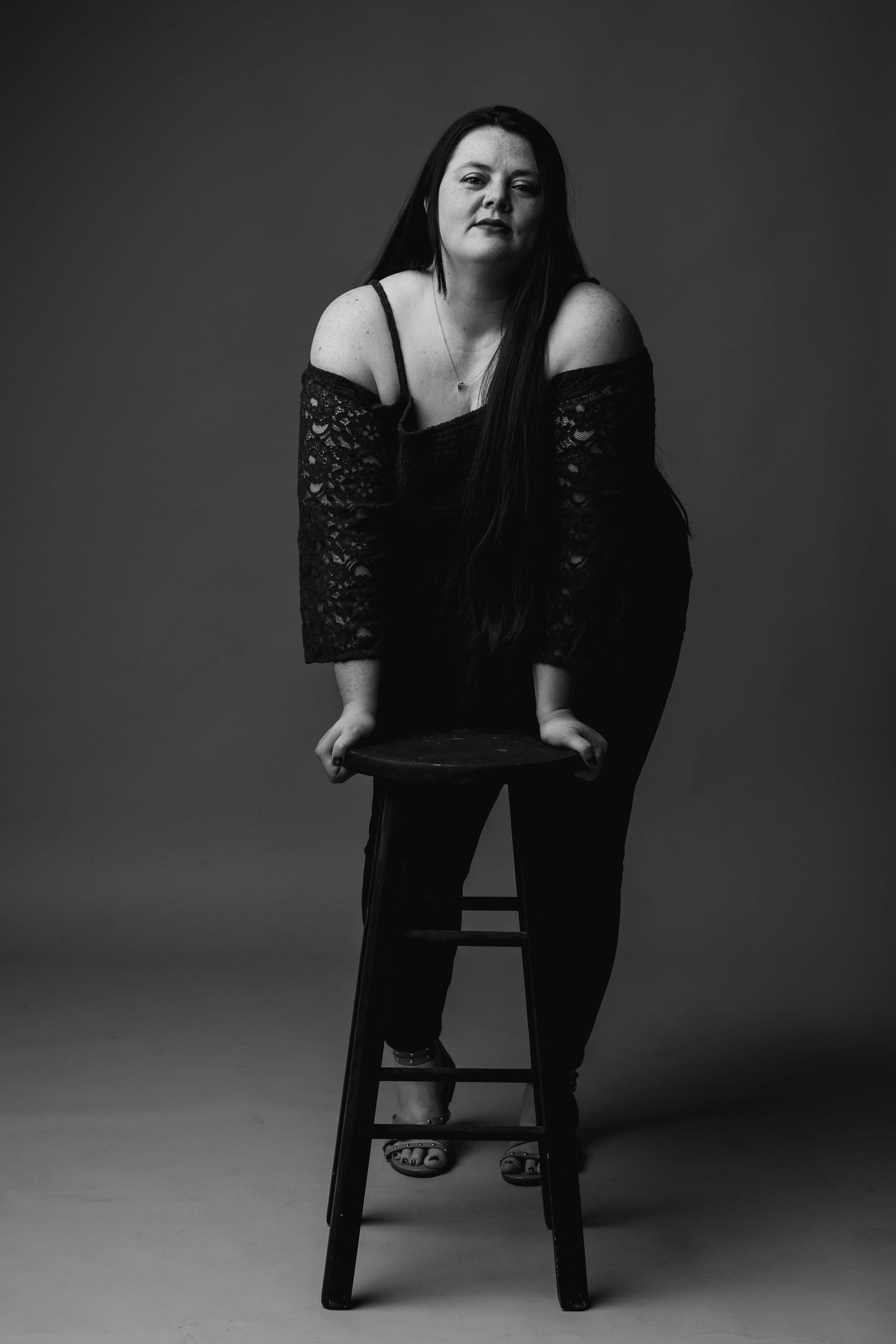 A gorgeous woman leans over stool and stares down the lens in a studio portrait in amarillo tx.