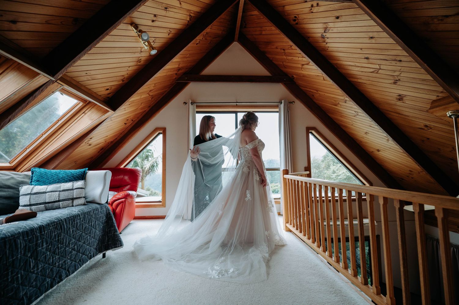 Wedding dress fitting in an attic room with exposed wooden beams and large windows.