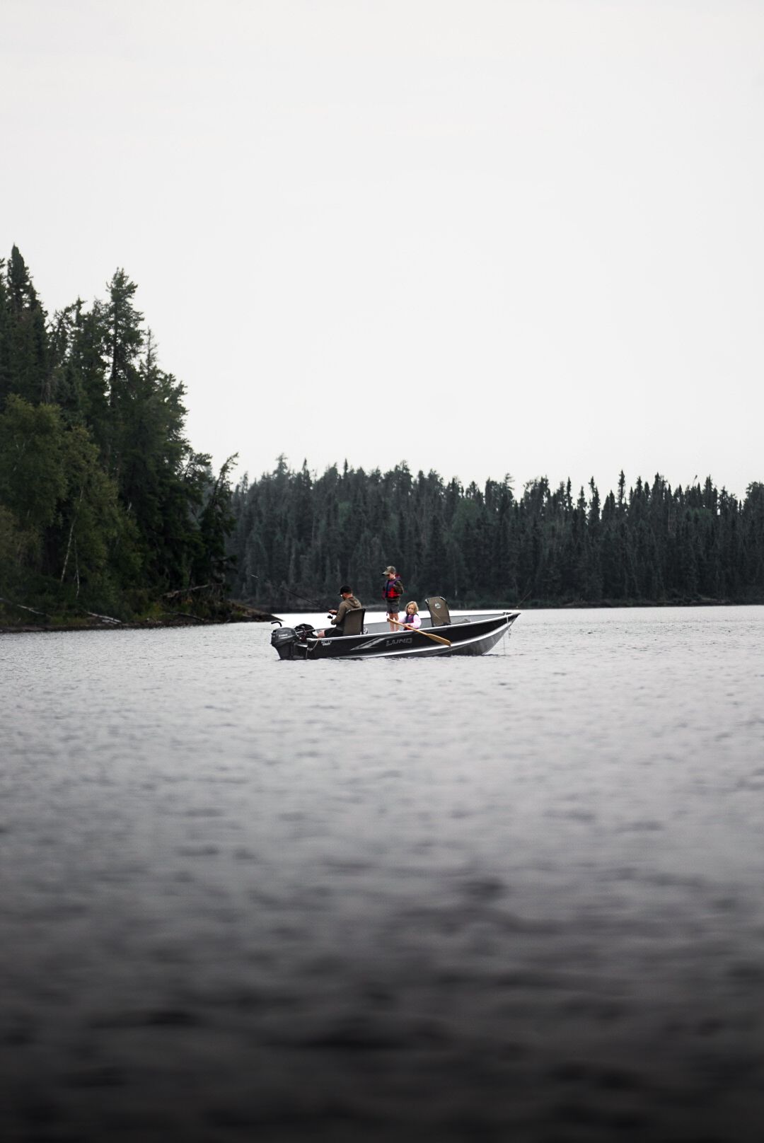 Small fishing boat glides across misty lake waters near forested shoreline.
