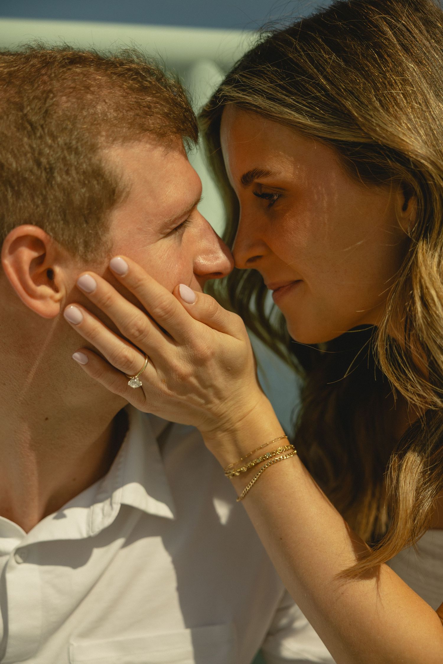 Romantic couple sharing an intimate moment, woman with engagement ring gently holding man's face close to hers.