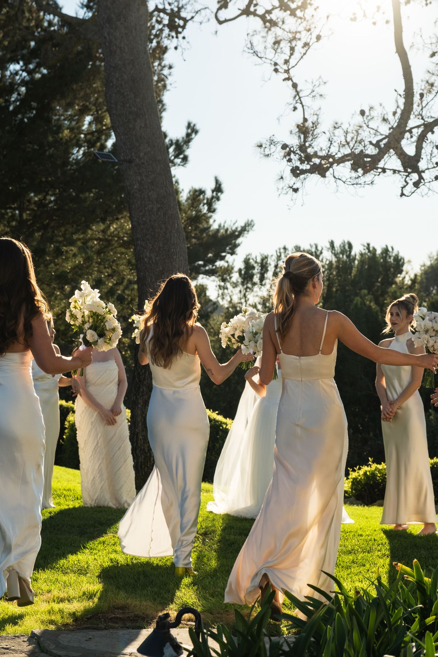 A group in white dresses stands together on a grassy hillside backlit by golden sunlight.