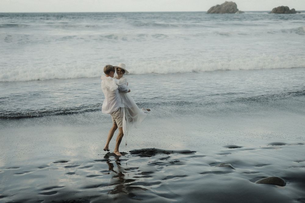 A person in a white dress walks along a misty beach shoreline at sunset creating a dreamy coastal scene.