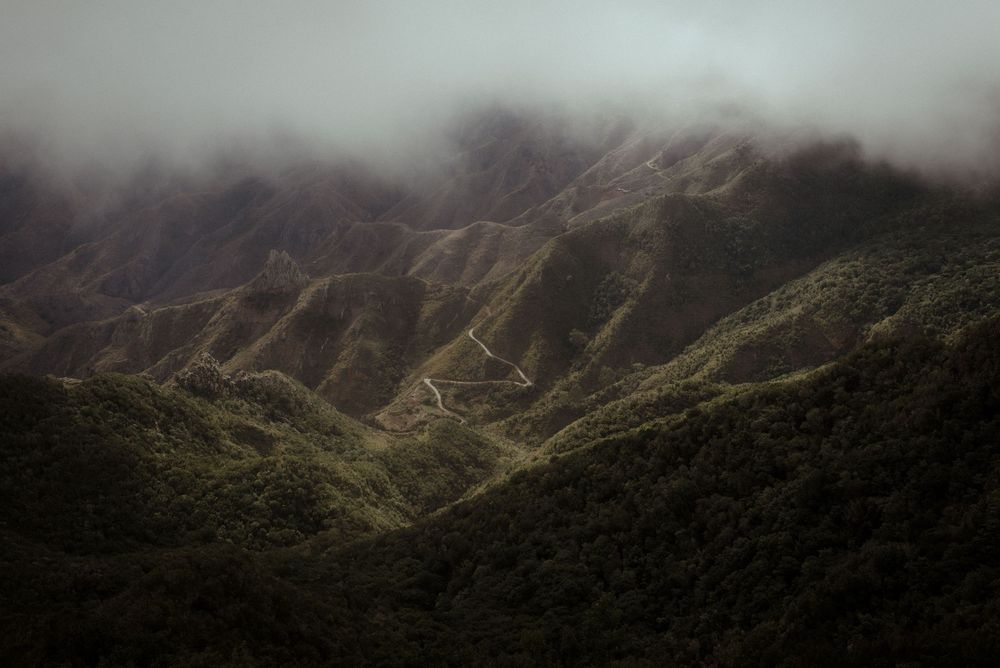Dramatic aerial view of lush green mountains shrouded in misty clouds stretching across a rugged tropical landscape.