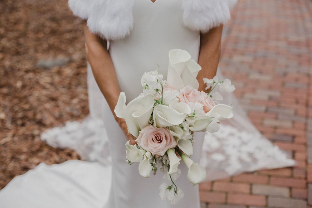 Delicate bridal bouquet with pink roses and white flowers against white wedding dress.