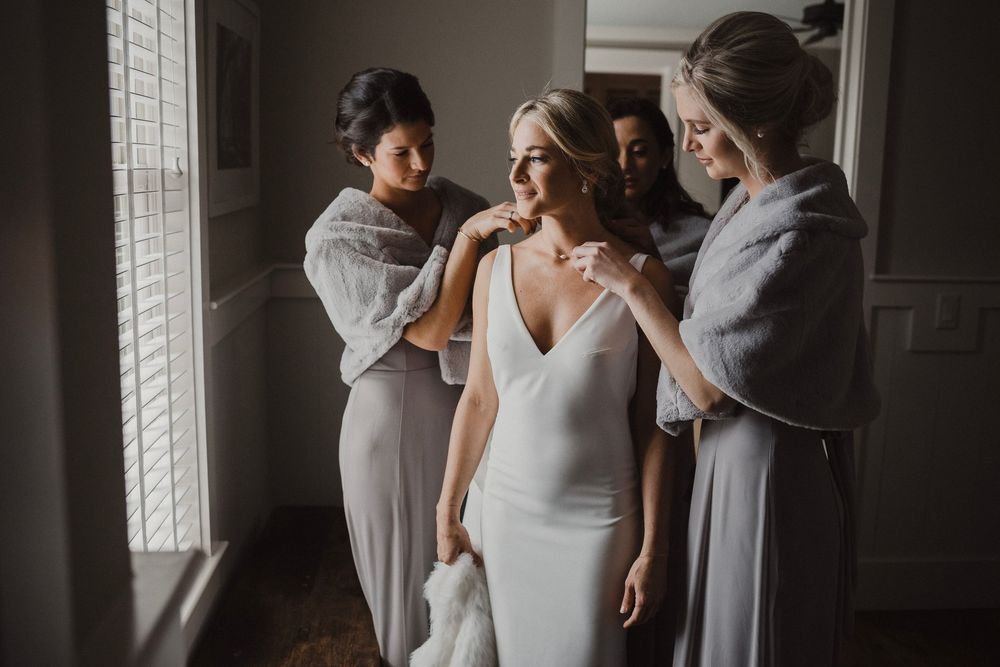 A group in light gray dresses helps prepare for a wedding in a sunlit room.