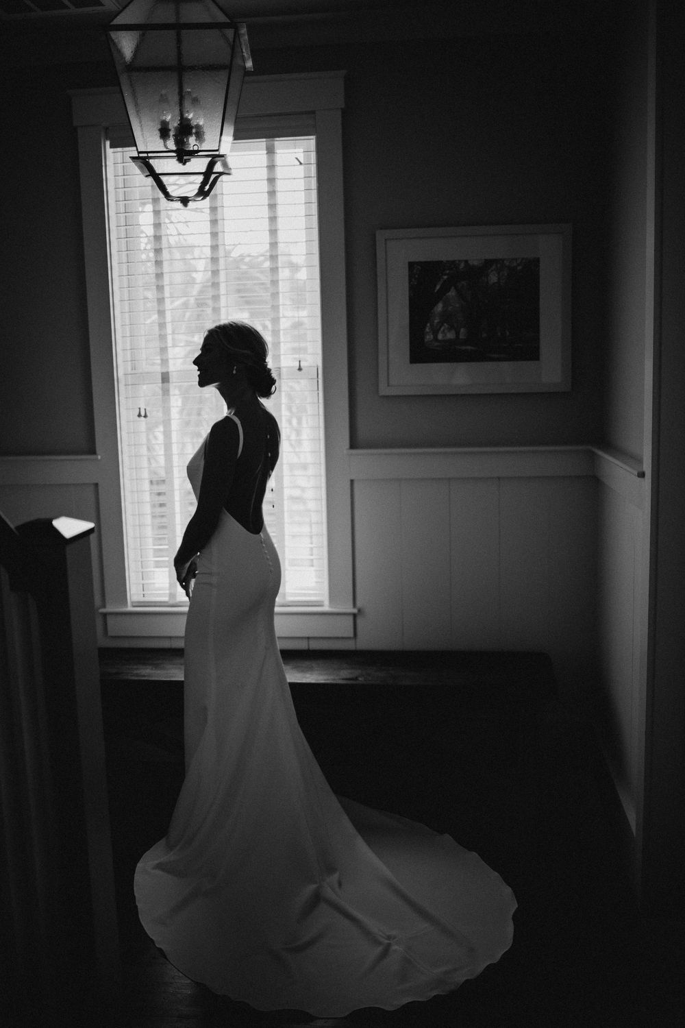 Dramatic black and white silhouettes show a bride twirling in her wedding dress by a window.