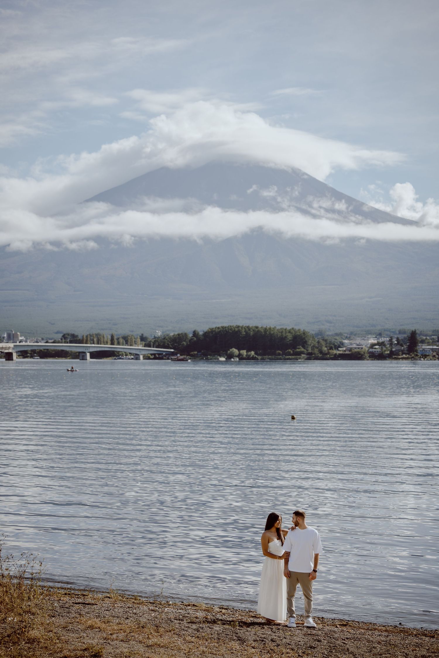 Mount Fuji rises majestically over Lake Kawaguchiko with a snowy peak and cloudy sky.