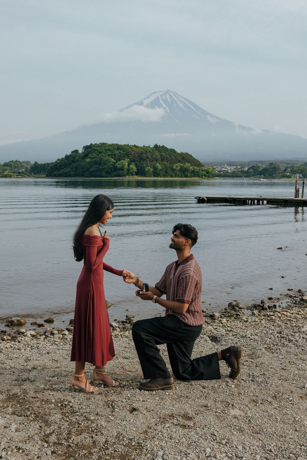 A romantic proposal scene unfolds on a rocky beach with Mount Fuji visible in the misty background.