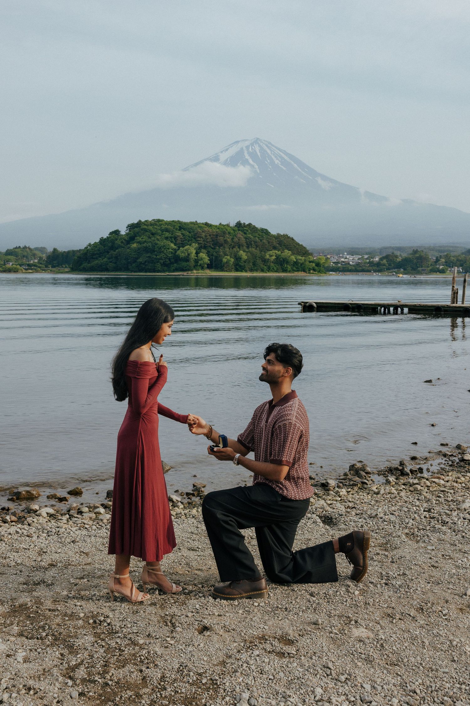A romantic proposal scene unfolds on a rocky beach with Mount Fuji visible in the misty background.