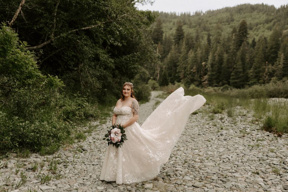Wedding party poses along a rocky riverbank with lush forest backdrop in natural outdoor setting.