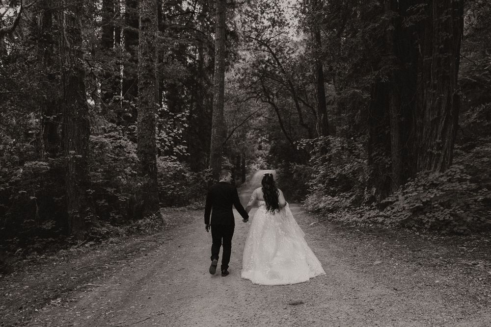 Black and white wedding photos taken on a tree-lined forest path during an intimate ceremony.