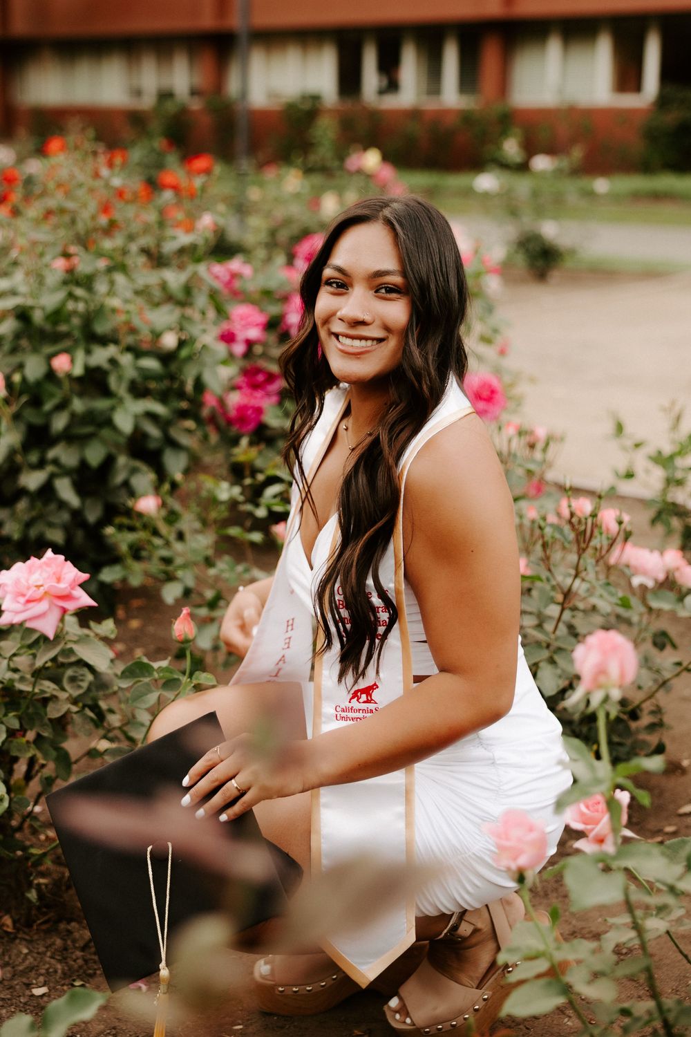 Woman posing in white dress among blooming rose bushes in a courtyard garden setting.