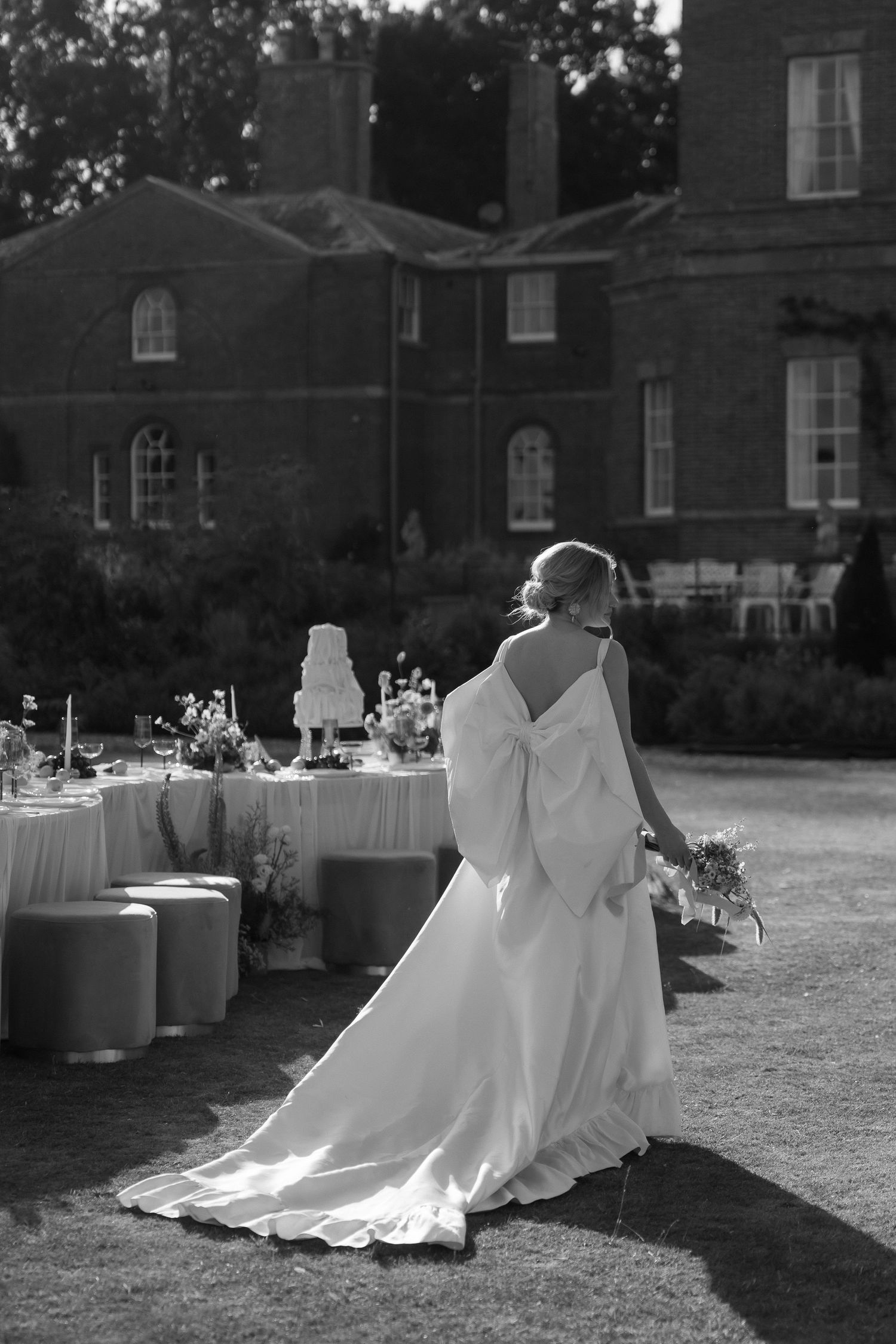 Black and white photo of an elegant wedding reception setup at a stately mansion with tables and decor on the lawn.