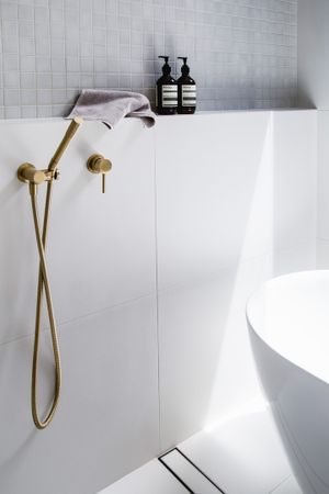 Minimalist bathroom detail featuring brass fixtures and white tile with dark bottles on shelf.