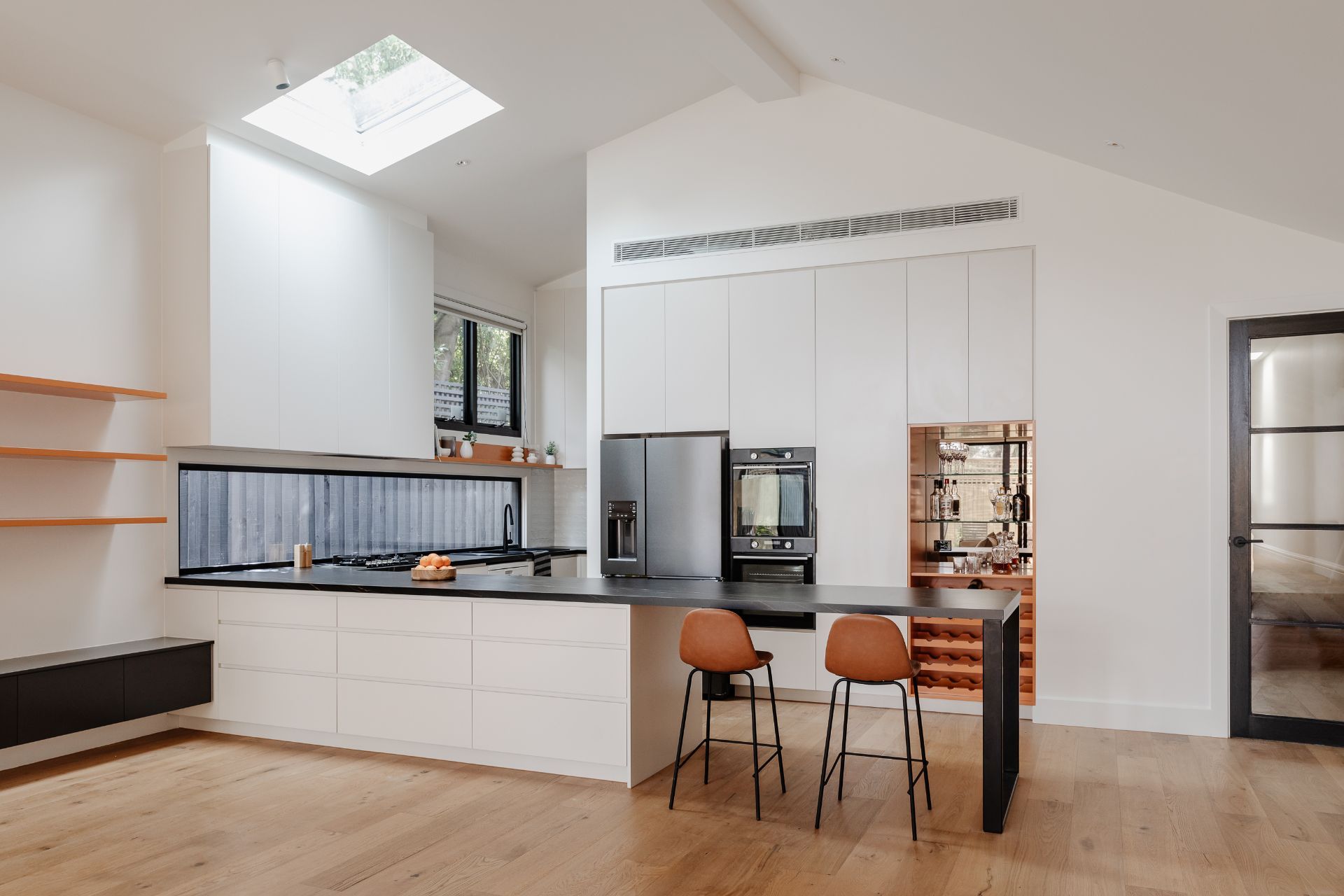 Modern kitchen with skylight features white cabinetry, wooden bar stools, and contemporary fixtures.