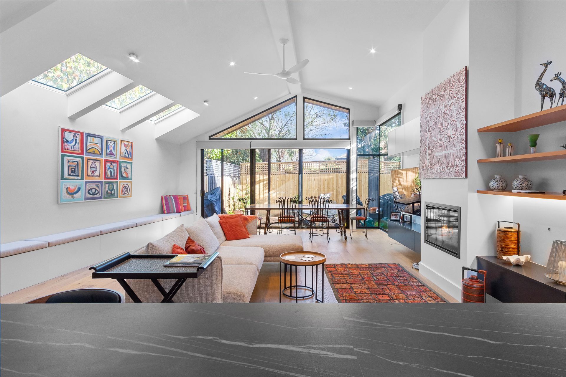 Bright open-concept living room with skylights, colorful decor, and large glass doors leading outdoors.