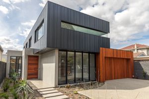 Contemporary house exterior with dark metal cladding, wooden gate, and geometric architecture.