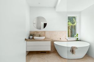 Serene bathroom with freestanding tub, round mirror, and natural stone tiles.