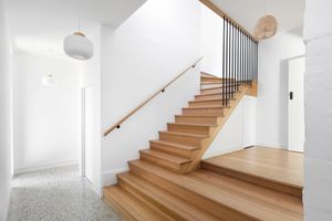 Modern wooden staircase with metal railings and white walls in bright entryway.