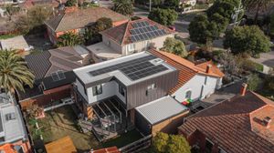 Aerial view of modern house with solar panels on roof surrounded by traditional tile-roofed homes.